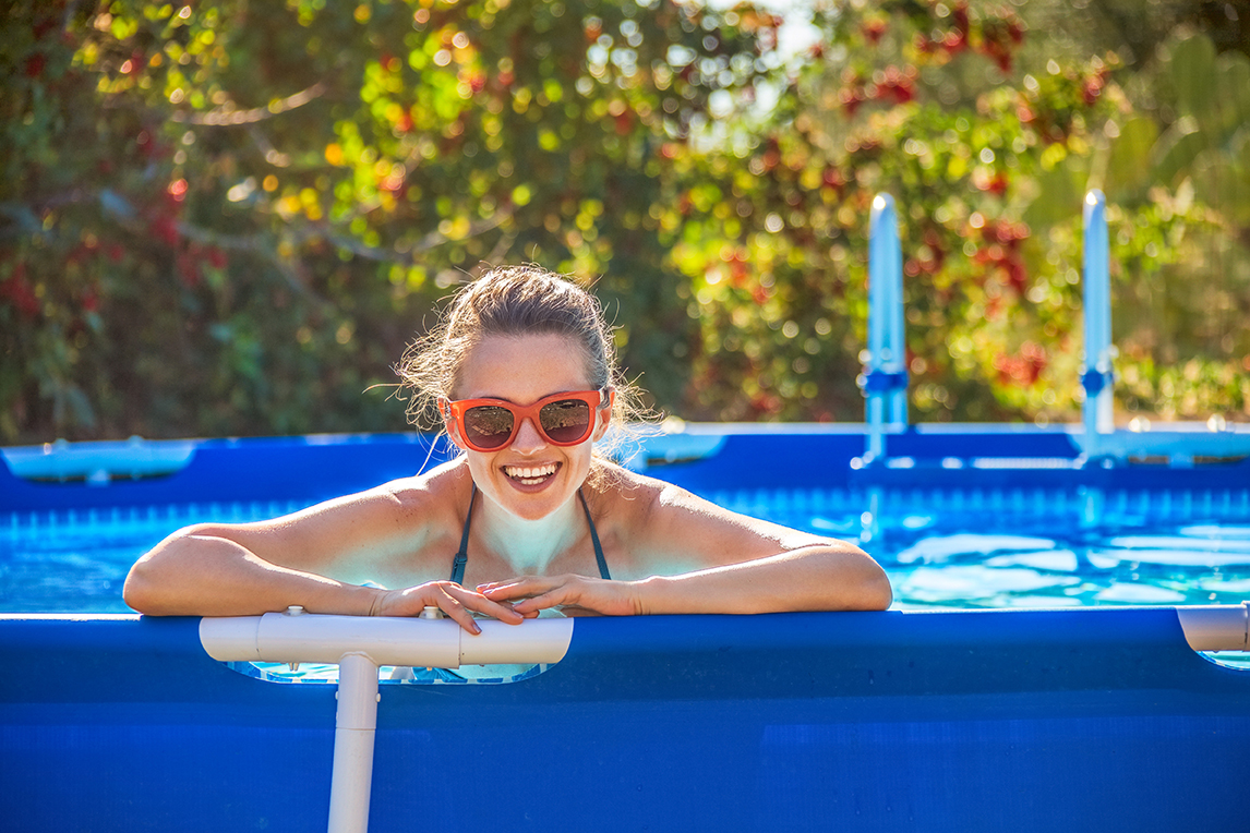 Woman Smiling and leaning up against the edge of an above ground pool.