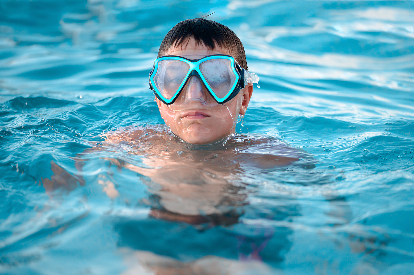 A child, a teenager in a swimming mask swims in clear blue water in a pool, pond or ocean, close-up.