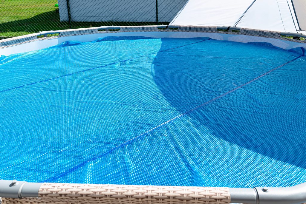 A large expansion pool with a diameter of 3.96 m, set in the yard next to the house, covered with a solar mat.